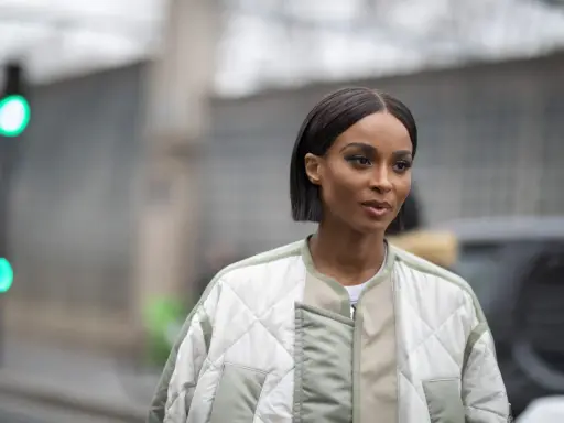 Une femme au regard intense arbore une coupe carré long impeccable, vêtue d'une veste matelassée tendance.