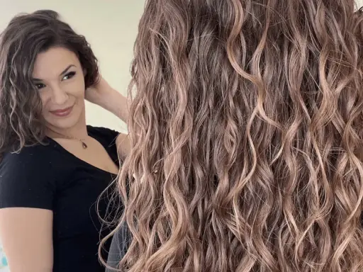 Une femme admire sa chevelure bouclée, résultat d'une décoloration subtile qui illumine ses ondulations naturelles.