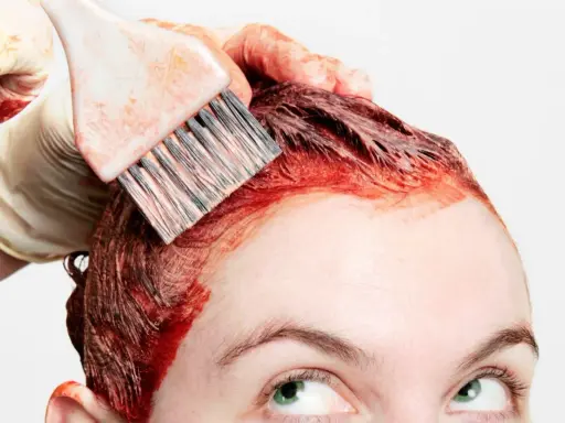 Application de teinture rouge sur les cheveux, étape clé de la routine cheveux colorés. Une main gantée utilise un pinceau pour une application précise.