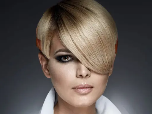 Une femme au regard intense arbore une coupe au bol audacieuse, avec des mèches blondes et des pointes orangées.