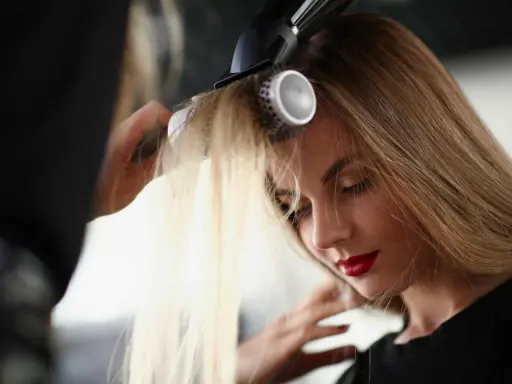Coiffure d'une femme aux cheveux blonds, mise en valeur par une frange rideau sur cheveux fins, sublimée par un brushing.