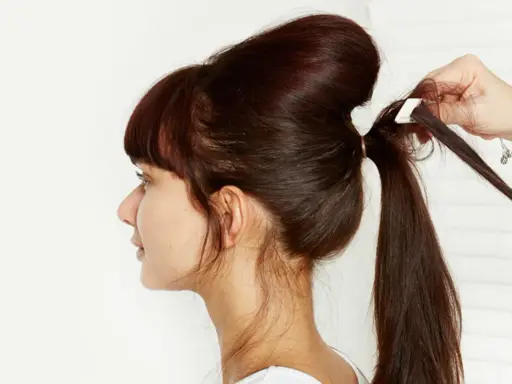 Une main ajuste une mèche pour créer un chignon sophistiqué. La coiffure volumineuse est en cours de réalisation.