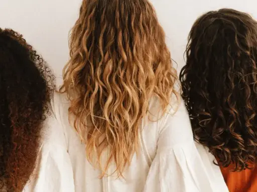 Trois femmes montrent leurs cheveux bouclés abîmés, de différentes couleurs et textures, sur fond blanc.