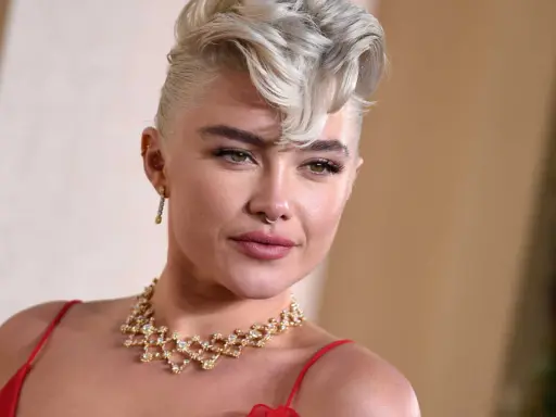 Une femme arbore une coupe courte blonde tendance, ornée d'un collier scintillant et d'une robe rouge.