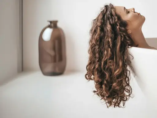 Une femme aux cheveux bouclés se détend dans une baignoire. Elle se demande combien de shampoing par lavage est idéal pour ses cheveux.