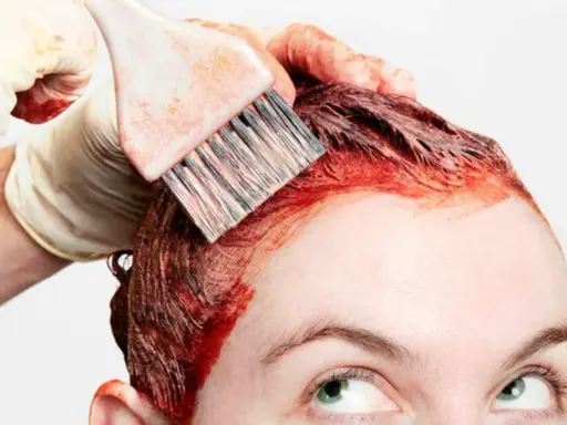 Application d'une teinture rouge pour un nouvel effet couleur cheveux. Une main gantée utilise un pinceau pour colorer les racines.