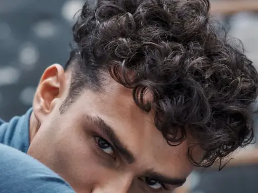 Gros plan sur un homme avec une coupe homme mi long bouclé, ses boucles sombres encadrant son visage.