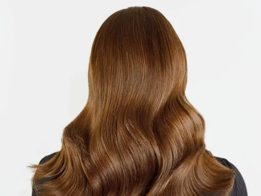 Chevelure brune aux reflets chauds, un balayage chatain clair subtil illumine ces ondulations douces.