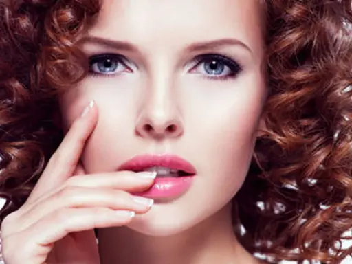 Une femme à la peau claire et aux yeux bleus, avec une chevelure rousse bouclée. Ses lèvres sont roses et brillantes.