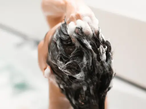 Mousse de shampoing sans silicone, une main masse le cuir chevelu sous une douche.