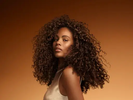 Une jeune femme aux cheveux bouclés et brillants, un exemple de comment bien rincer ses cheveux pour un éclat naturel.