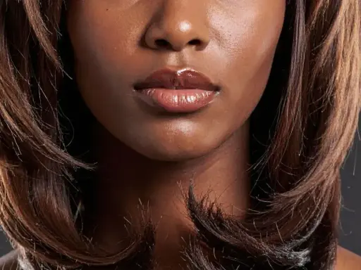 Bouche pulpeuse et brillants, encadrée par un dégradé cheveux long brun, aux reflets chauds.