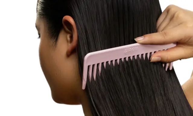 Une main peigne de longs cheveux noirs avec un peigne rose. Pas de nœud dans les cheveux, juste une chevelure soyeuse.