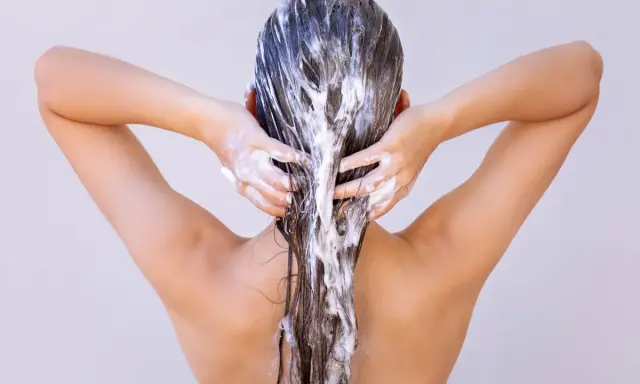 Dos mains appliquent un masque capillaire sur des cheveux longs et bruns. Attention à ne pas laisser poser un masque cheveux trop longtemps !
