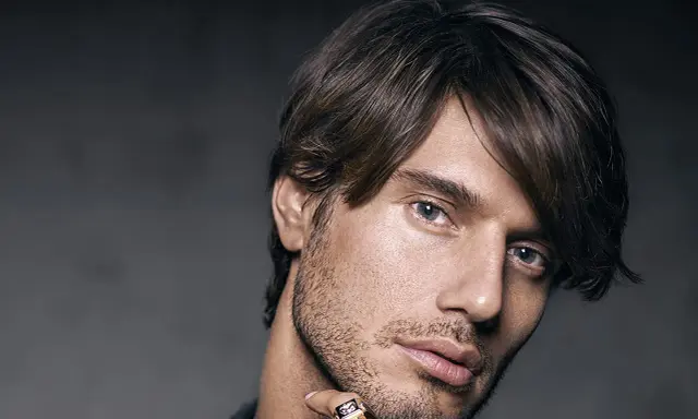 Un homme au regard intense, coiffé décoiffé, porte une bague ornée d'un motif discret.