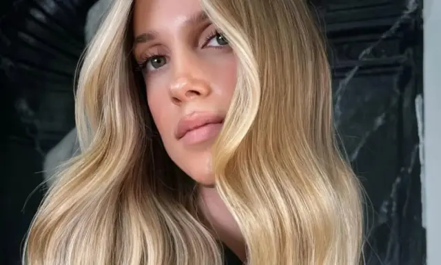 Une femme aux yeux verts et aux lèvres pulpeuses arbore une chevelure ondulée d'une magnifique teinte de blond.