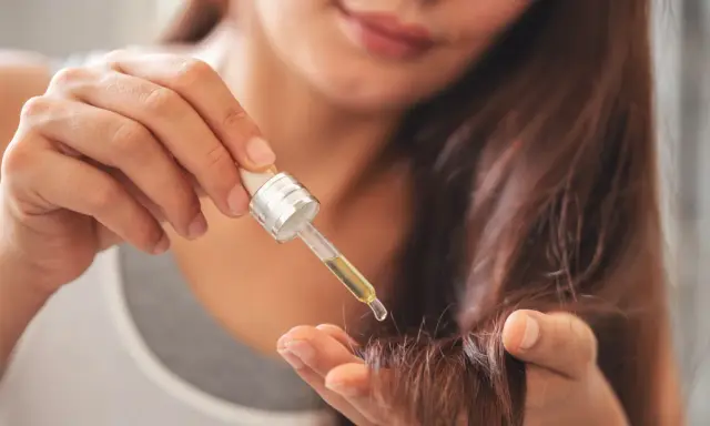 Une main applique une goutte d'huile sur la pointe des cheveux pour les nourrir.