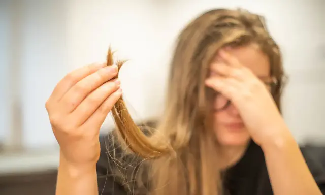 Une main tient une mèche de cheveux, visiblement abîmés, comme si c'était du cheveux mort. La personne semble désespérée.