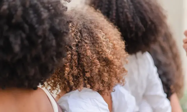 Trois femmes avec de magnifiques cheveux frisés, un mélange de bruns foncés et de châtain clair, se tiennent côte à côte.