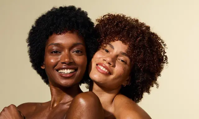 Deux femmes souriantes, l'une avec des cheveux crépus 4c noirs, l'autre avec des boucles rousses.