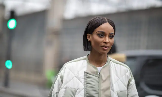 Une femme au regard intense arbore une coupe carré long impeccable, vêtue d'une veste matelassée tendance.