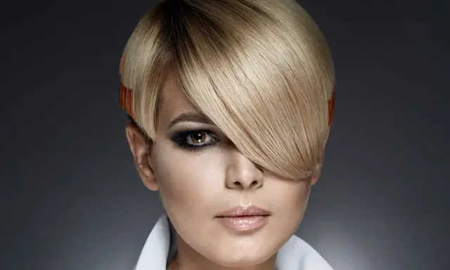 Une femme au regard intense arbore une coupe au bol audacieuse, avec des mèches blondes et des pointes orangées.