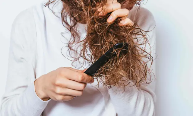 Une personne démêle ses cheveux mouillés et **cheveux emmêlés à la racine** avec un peigne noir.