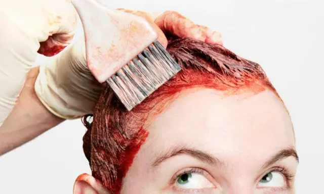 Application d'une teinture rouge pour un nouvel effet couleur cheveux. Une main gantée utilise un pinceau pour colorer les racines.