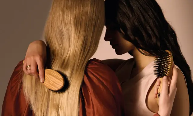 Deux femmes se serrent, l'une brosse les cheveux blonds de l'autre avec une brosse en bois.