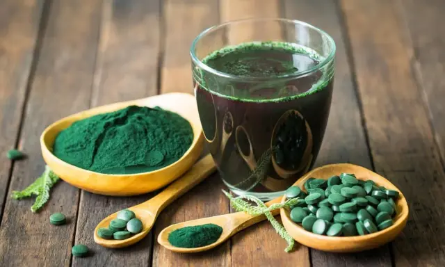 Spiruline en poudre, comprimés et boisson verte sur fond de bois. Découvrez les bienfaits spiruline cheveux pour une chevelure éclatante.