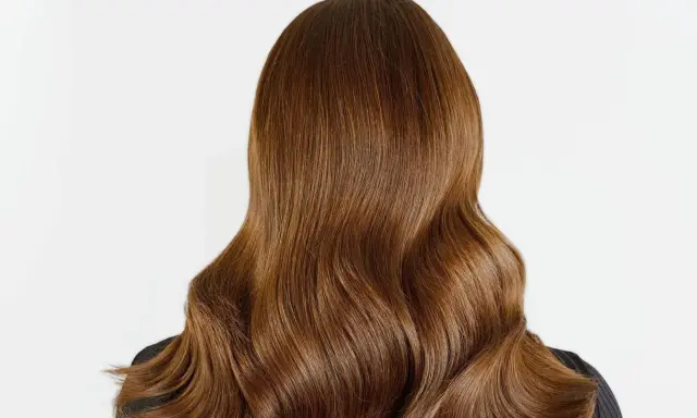 Chevelure brune aux reflets chauds, un balayage chatain clair subtil illumine ces ondulations douces.