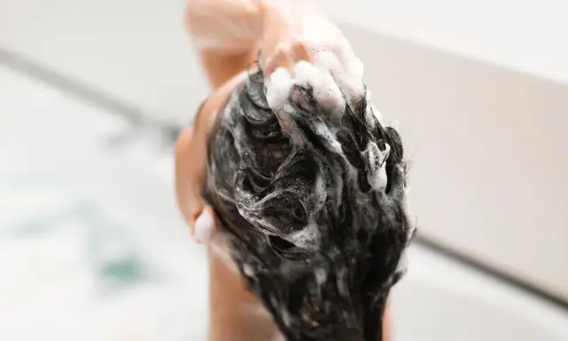 Mousse de shampoing sans silicone, une main masse le cuir chevelu sous une douche.