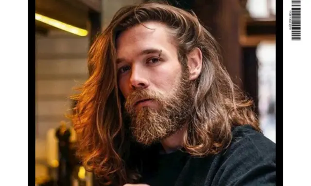 Un homme avec une barbe et de longs cheveux ondulés, parfait pour un projet cheveux long homme.