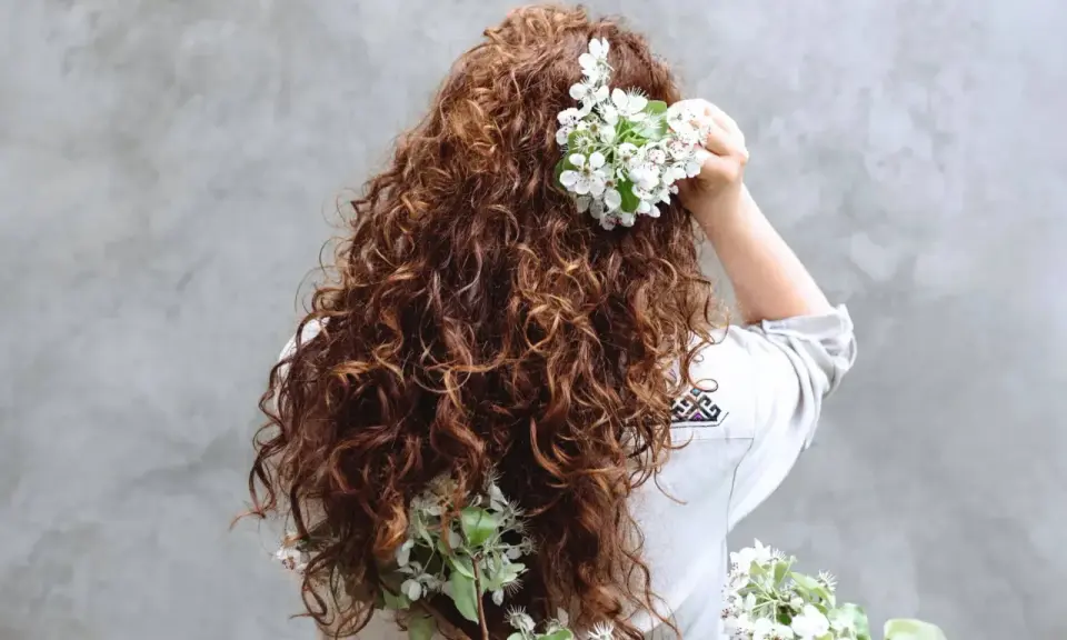Chevelure brune et bouclée ornée de fleurs blanches, évoquant un décollement de racine naturel et printanier.