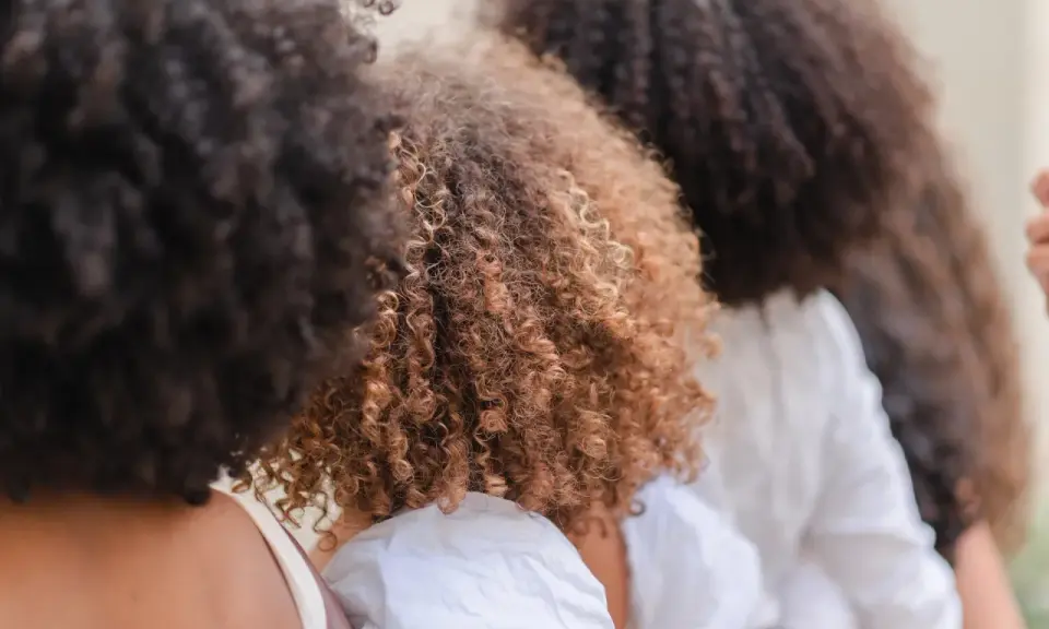 Trois femmes avec de magnifiques cheveux frisés, un mélange de bruns foncés et de châtain clair, se tiennent côte à côte.