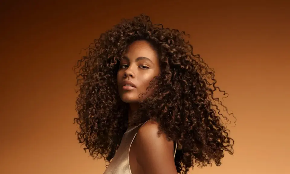 Une jeune femme aux cheveux bouclés et brillants, un exemple de comment bien rincer ses cheveux pour un éclat naturel.