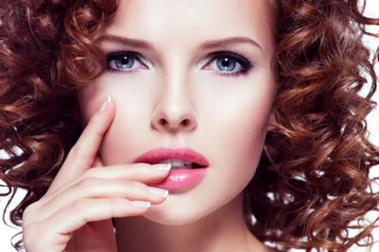 Une femme à la peau claire et aux yeux bleus arbore une chevelure rousse bouclée. La couleur de cheveux parfaite pour sa peau claire et ses yeux bleus.