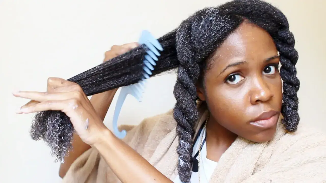 Une femme applique un soin sur ses cheveux, les peignant avec un peigne bleu. Ses cheveux sont torsadés en un gros noeud dans les cheveux.