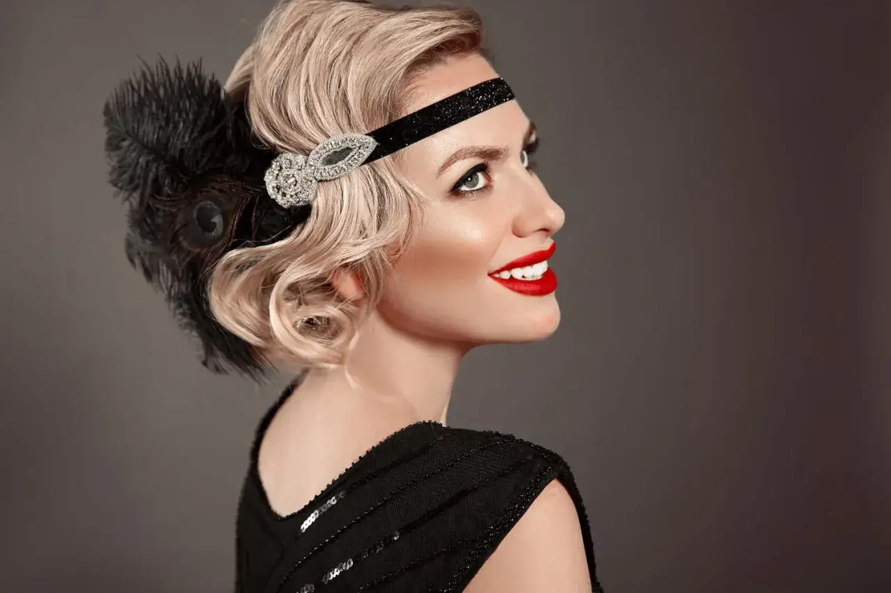 Coiffure ann&eacute;e 20 cheveux long, avec bandeau orn&eacute; de plumes et de strass. Rouge &agrave; l&egrave;vres &eacute;clatant.