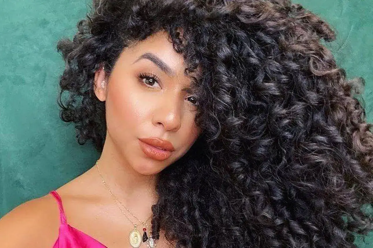 Une femme au regard intense, ses cheveux boucl&eacute;s tombent en cascade. Elle porte un collier fin et une robe rose. Mes cheveux ne bouclent pas partout, mais j'adore cette texture !