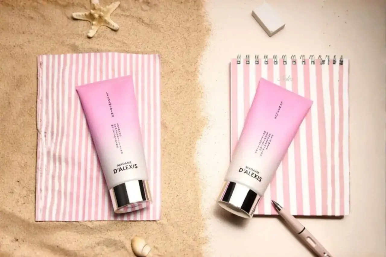 Deux tubes de cr&egrave;me rose p&acirc;le, une solution pour cheveux secs, sur des serviettes ray&eacute;es, entour&eacute;s de sable et d'une &eacute;toile de mer.