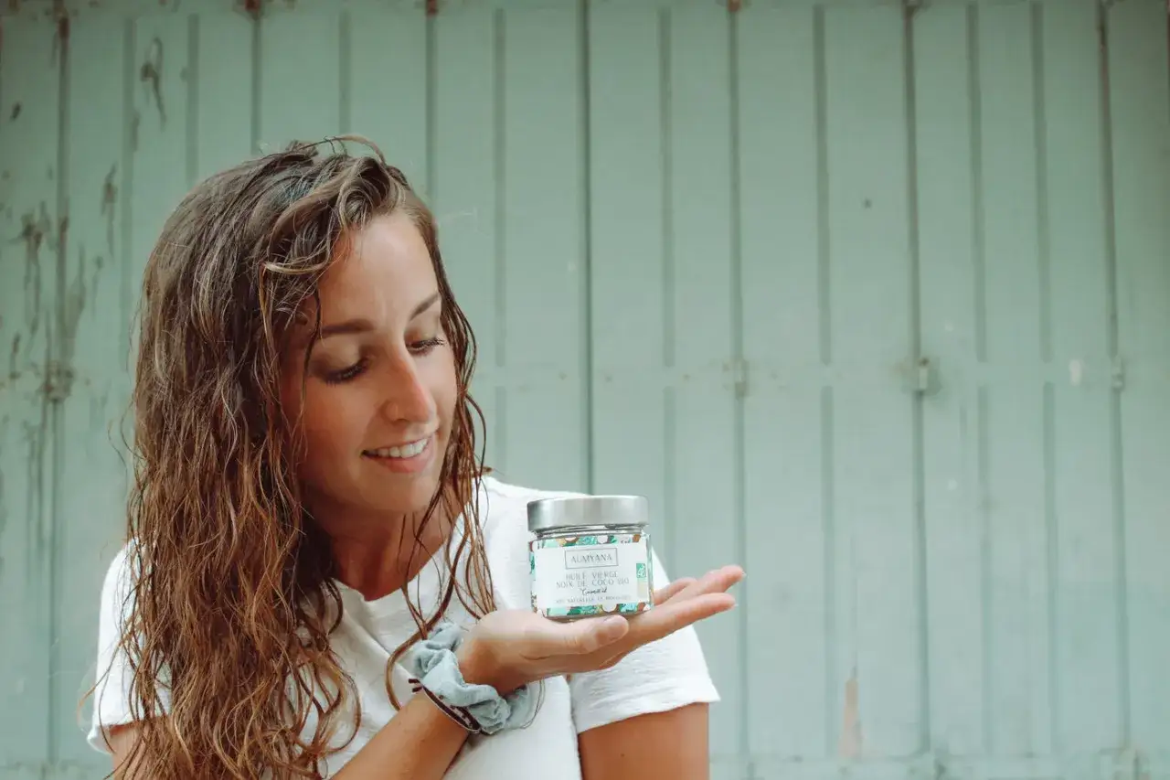 Une jeune femme aux cheveux bouclés tient un pot d'huile de coco bio, un secret pour des boucles sublimes et naturelles.
