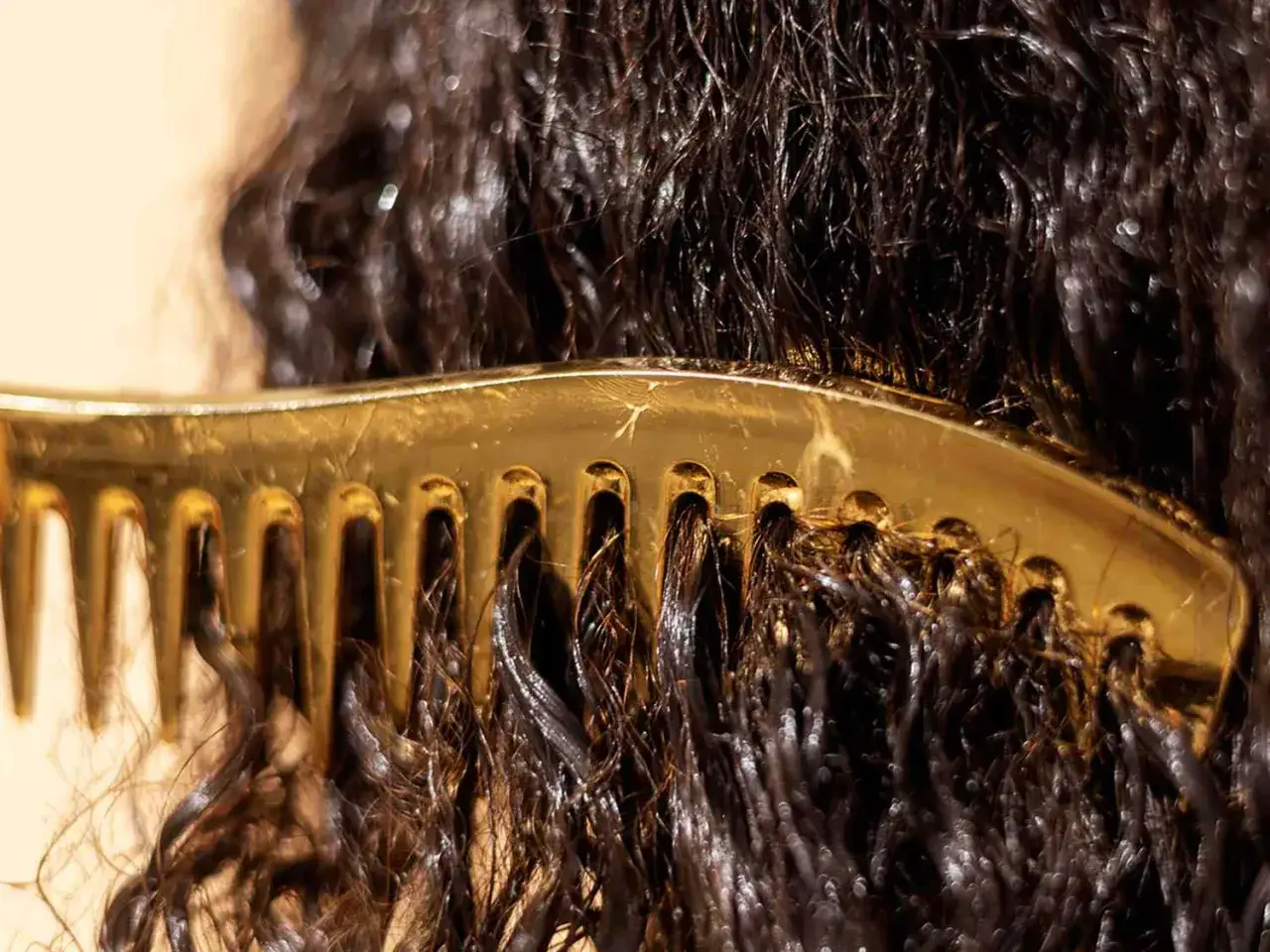 Un peigne doré démêle doucement les pointes de cheveux sombres et ondulés, révélant leur texture naturelle.