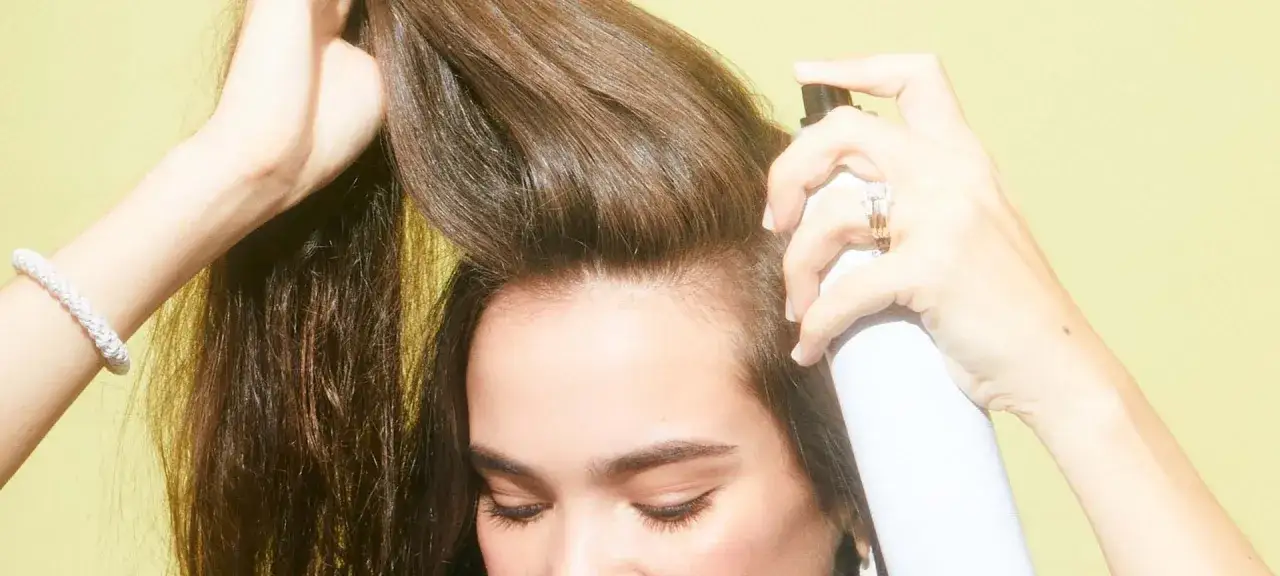 Une femme applique de la laque sur ses cheveux. Est-ce que la laque abîme les cheveux ? La réponse dépend de la fréquence et du type de produit utilisé.