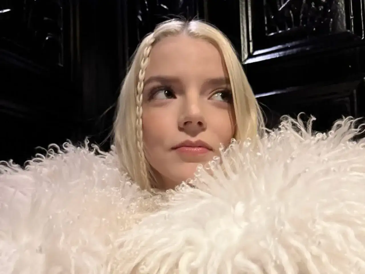 Une femme blond platine, le regard perdu dans le lointain, enveloppée dans une épaisse fourrure blanche.