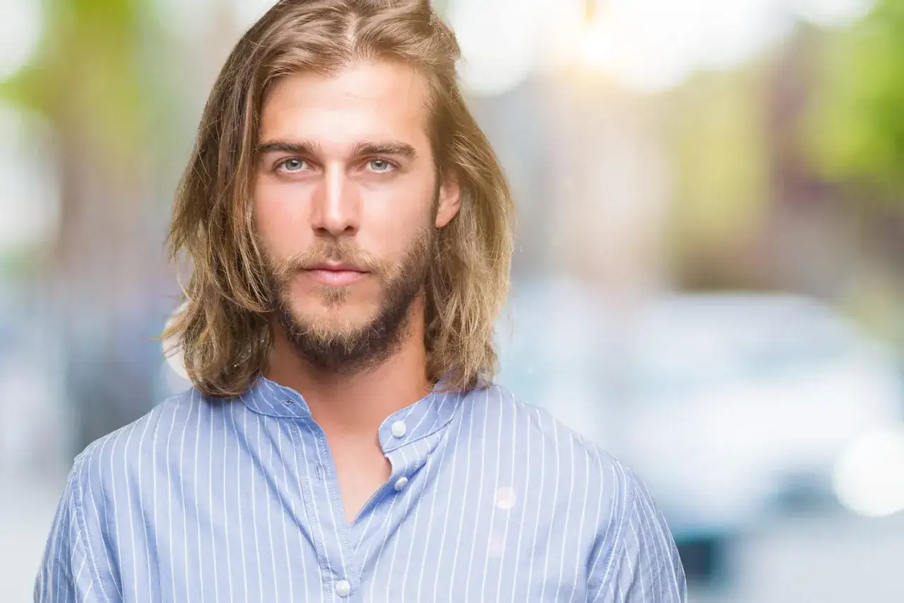 Un homme au regard intense, ses longs cheveux blonds flottent. Un style qui pourrait inspirer un projet cheveux long homme.