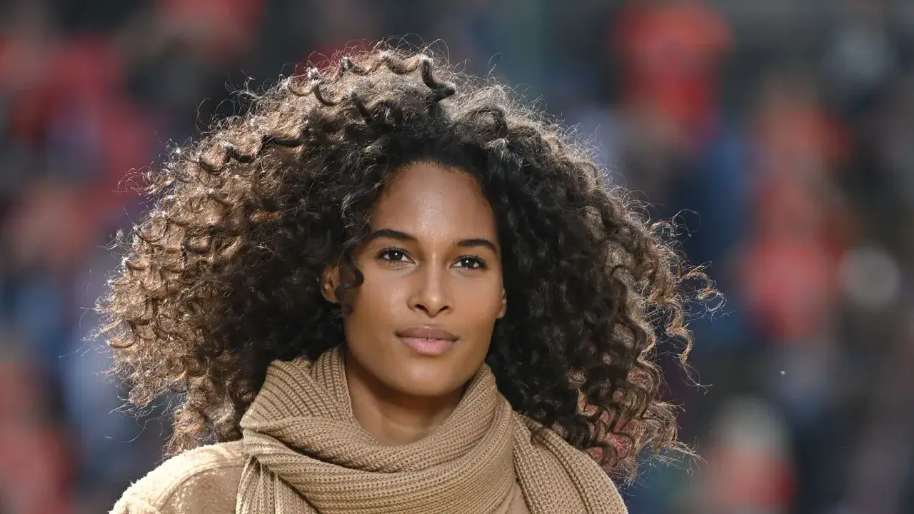 Une femme au regard doux arbore une magnifique coupe cheveux fris&eacute;s, encadrant son visage avec des boucles naturelles et volumineuses.