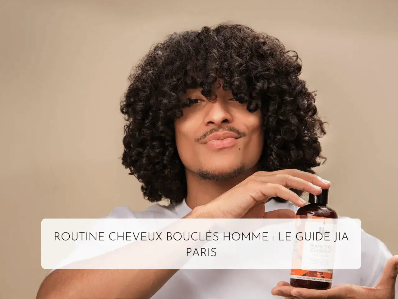 Homme aux magnifiques cheveux 3c, tenant un flacon de shampoing clarifiant.