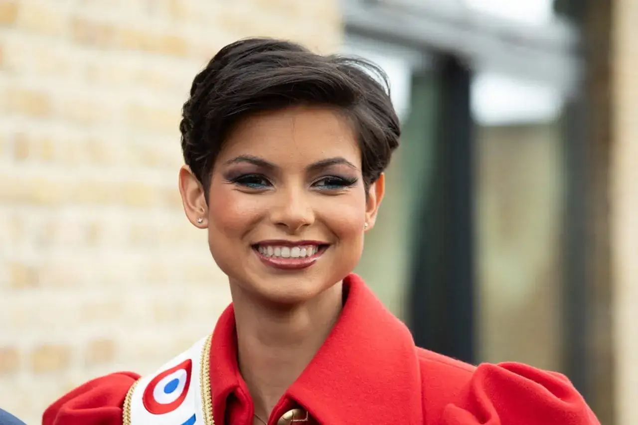 Une jeune femme souriante avec une coiffure plaqué, un maquillage bleu vif et une écharpe tricolore.