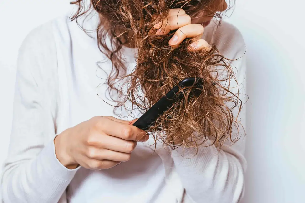 Une personne peigne ses cheveux mouill&eacute;s, qui sont visiblement emm&ecirc;l&eacute;s &agrave; la racine.